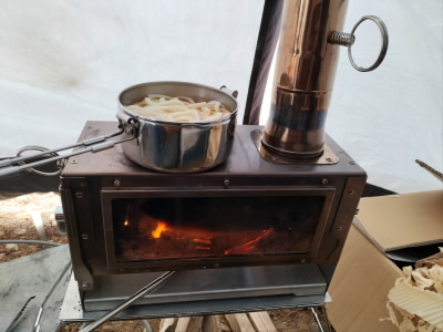 お昼はおうどん。
それに網を置いて、餅を焼きました。
煙突についているわっかはダンパーの調整用です。
これを回して煙突へ抜ける空気を調整することによって、流入する空気量を調整できます。
これがないと、一気に燃えてしまうことがあり、燃費が悪くなります。